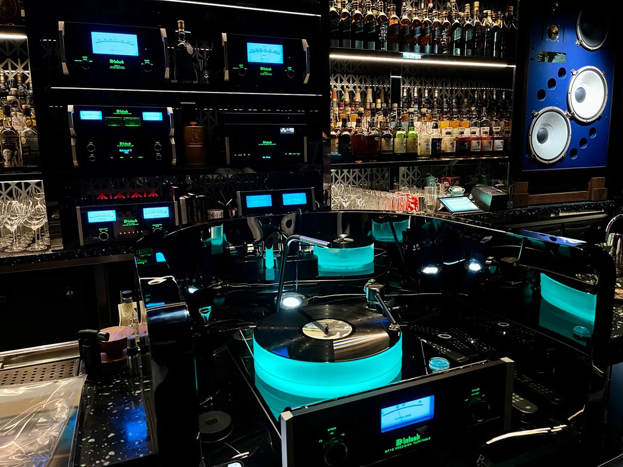 A wall of McIntosh amplifiers with glowing blue meters among the bottles at a bar.